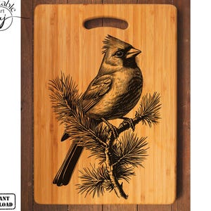 May include: A wooden cutting board with a laser engraved design of a cardinal bird perched on a pine branch. The design is in black and brown on a natural wood background.