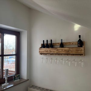 Puede incluir: Un botellero de madera montado en la pared, con varias botellas de vino oscuras y copas de vino transparentes. El botellero es de madera marr&oacute;n claro y tiene un dise&ntilde;o r&uacute;stico. Las copas cuelgan debajo.