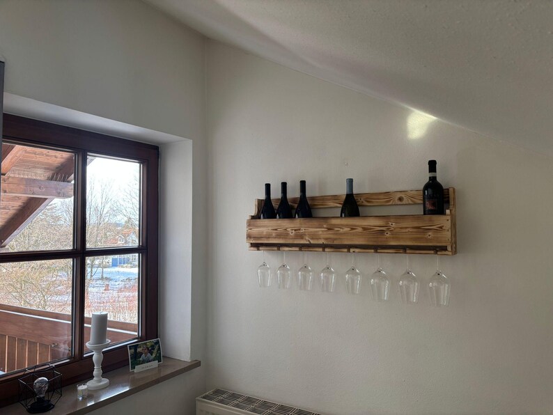 Puede incluir: Un botellero de madera montado en la pared, con varias botellas de vino oscuras y copas de vino transparentes. El botellero es de madera marr&oacute;n claro y tiene un dise&ntilde;o r&uacute;stico. Las copas cuelgan debajo.