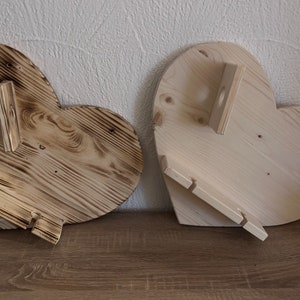 May include: Two wooden heart-shaped shelves with a rustic finish. One shelf has a natural wood color and the other has a darker, burnt wood finish. Both shelves have a small, rectangular shelf attached to the side.