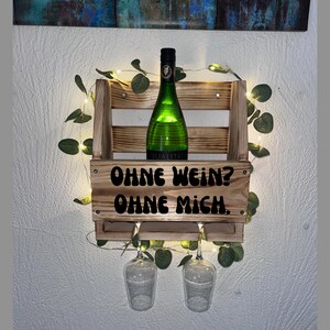 Puede incluir: Estante de vino de madera con una botella de vino verde y dos copas de vino. El estante tiene el texto "OHNE WEIN? OHNE MICH." El estante est&aacute; decorado con vegetaci&oacute;n y luces de hadas.
