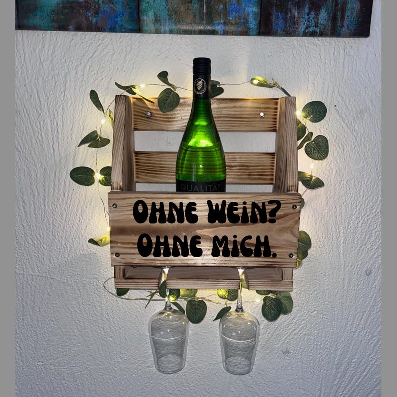 Puede incluir: Estante de vino de madera con una botella de vino verde y dos copas de vino. El estante tiene el texto "OHNE WEIN? OHNE MICH." El estante est&aacute; decorado con vegetaci&oacute;n y luces de hadas.