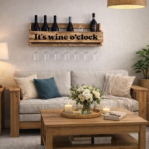 Puede incluir: Un botellero de madera con el texto "It's wine o'clock" sostiene botellas y copas de vino. El botellero est&aacute; sobre un sof&aacute; con cojines. Una mesa de centro con velas y flores completa la escena.