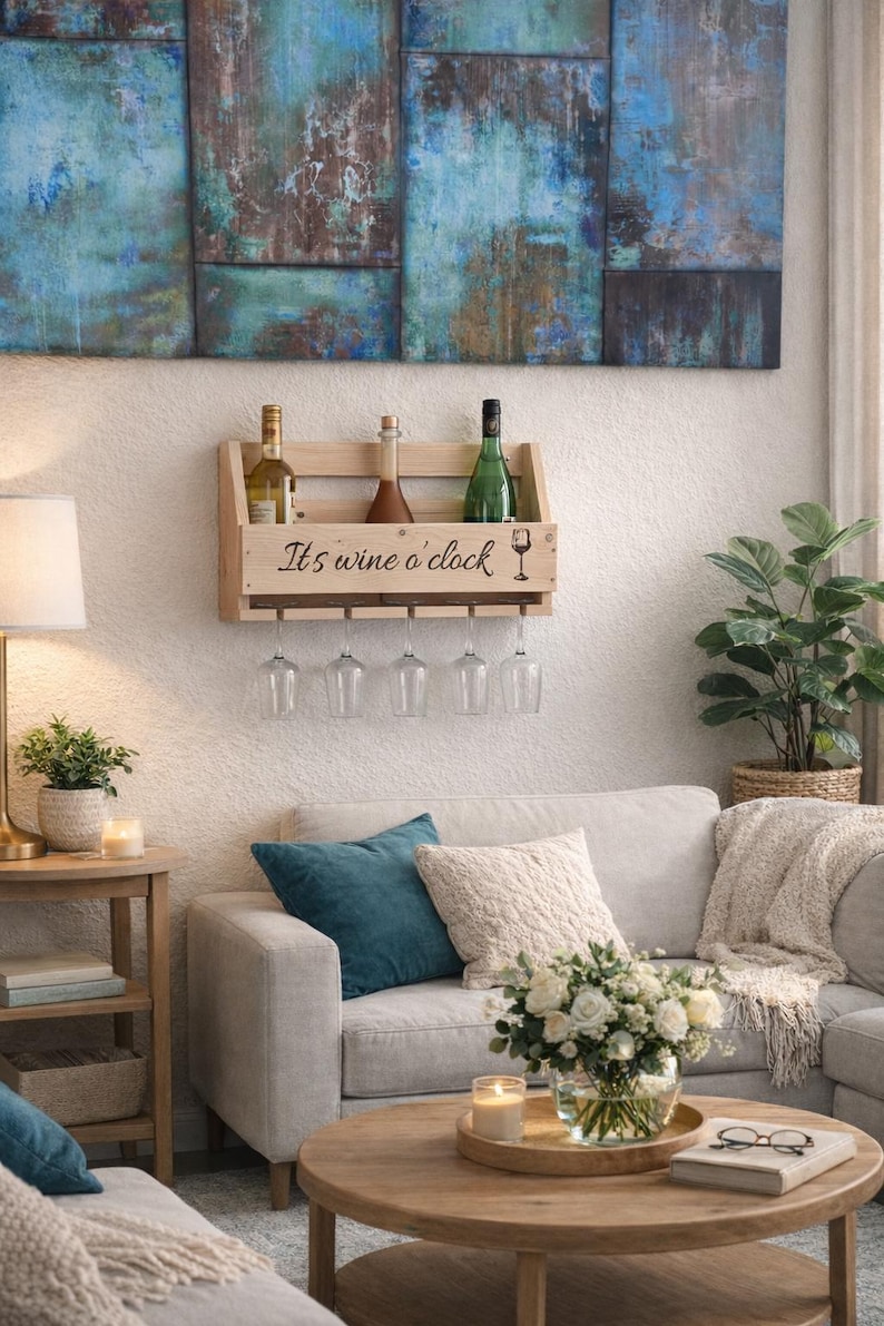 Puede incluir: Un botellero de vino de madera con el texto "It's wine o'clock" y un gr&aacute;fico de copa de vino. El botellero tiene capacidad para tres botellas de vino y tiene una fila de copas de vino colgantes. El fondo presenta un sal&oacute;n con un sof&aacute;, una mesa de centro y obras de arte.