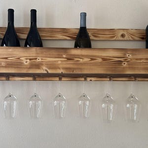 Puede incluir: Un botellero de madera r&uacute;stico, montado en la pared, con botellas de vino y copas de vino transparentes. El botellero est&aacute; dise&ntilde;ado para almacenar y exhibir vino y cristaler&iacute;a, con capacidad para varios art&iacute;culos.
