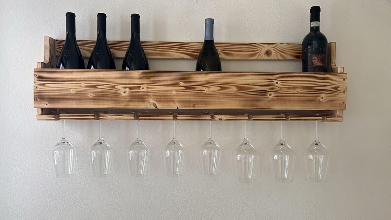 Puede incluir: Un botellero de madera r&uacute;stico, montado en la pared, con botellas de vino y copas de vino transparentes. El botellero est&aacute; dise&ntilde;ado para almacenar y exhibir vino y cristaler&iacute;a, con capacidad para varios art&iacute;culos.