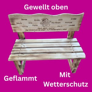 May include: A wooden bench with a wavy top and a slatted seat. The bench is made of light brown wood with a flamed finish. The backrest features a snake illustration and several names. Text on the bench includes "Gewellt oben", "Geflammt", and "Mit Wetterschutz".