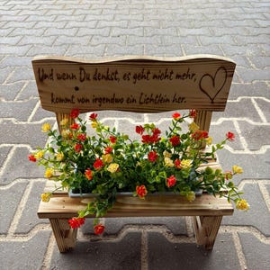 K&ouml;nnte beinhalten: Ein kleiner Holzbank-Blumentopf mit R&uuml;ckenlehne. Die R&uuml;ckenlehne tr&auml;gt den Text "Und wenn Du denkst, es geht nicht mehr, kommt von irgendwo ein Lichtlein her." und ein Herz. Die Bank enth&auml;lt einen Pflanztopf mit roten und gelben Blumen.