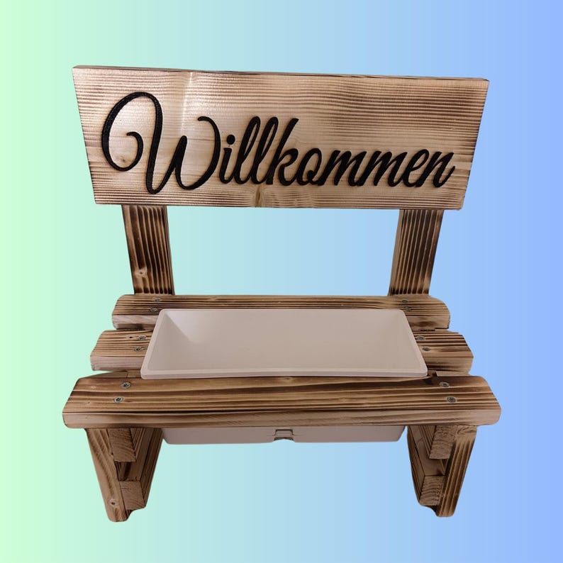 K&ouml;nnte beinhalten: Eine rustikale Holzbank mit dem Wort "Willkommen" in schwarzer Schrift. Die Bank hat eine rechteckige wei&szlig;e Schale und ist aus hellbraunem Holz mit sichtbarer Maserung gefertigt.