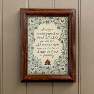 May include: A framed print with a dark brown wooden frame. The print features a floral border with hearts and a house illustration. The text reads: "if only I could give her back all she's given me. she makes her house in to a home and us, a family."