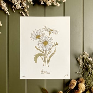May include: A botanical illustration of a bouquet of white daisies with yellow centers, drawn in gold and green ink on a white background. The print is titled "Daisy" and numbered "No. 7".