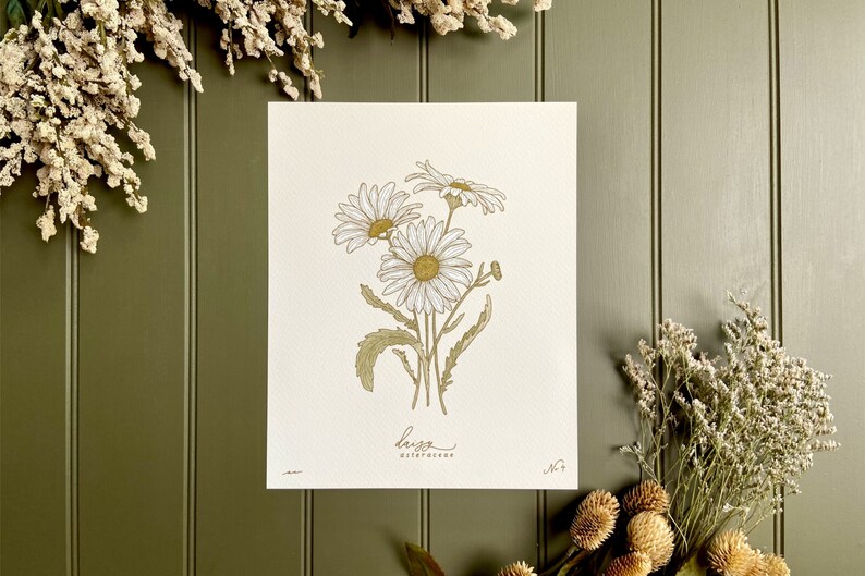 May include: A botanical illustration of a bouquet of white daisies with yellow centers, drawn in gold and green ink on a white background. The print is titled "Daisy" and numbered "No. 7".