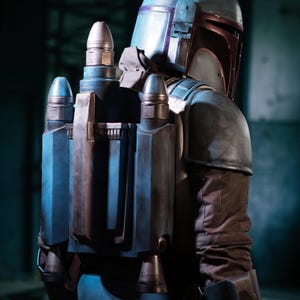 Puede incluir: Vista detallada de un casco y mochila propulsora mandalorianos. El casco es principalmente azul con detalles granates y una antena plateada. La mochila es azul y plateada con detalles cilíndricos. El disfraz tiene una apariencia desgastada.