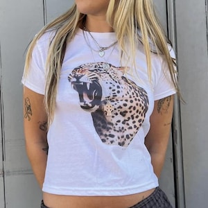 May include: White cropped t-shirt featuring a graphic print of a roaring leopard. The shirt has a relaxed fit and short sleeves.