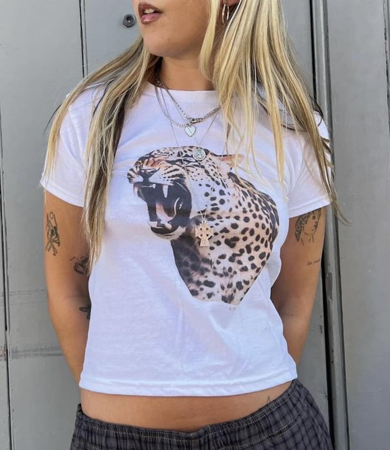 May include: White cropped t-shirt featuring a graphic print of a roaring leopard. The shirt has a relaxed fit and short sleeves.