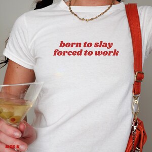 May include: White t-shirt with red text that reads "born to slay forced to work".
