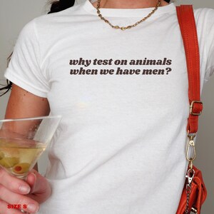 May include: White t-shirt with the text "why test on animals when we have men?" printed in brown.