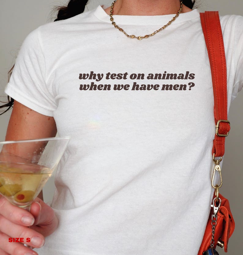 May include: White t-shirt with the text "why test on animals when we have men?" printed in brown.
