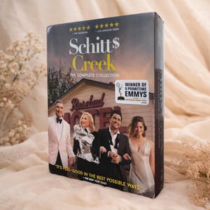 May include: A DVD box set of the television show "Schitt's Creek: The Complete Collection." The cover features the cast in front of the Rosebud Motel. The box set is labeled as a winner of 9 Primetime Emmys.