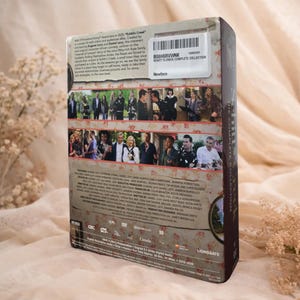 May include: A DVD box set of the television show "Schitt's Creek: The Complete Collection." The box set features images of the cast and the show's title. The packaging has a floral design and a white sticker with a barcode.