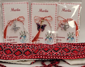 Pode incluir: Três pulseiras de corda vermelha e branca com pingentes de borboleta. As pulseiras estão embaladas em sacos de plástico transparentes com cartões brancos que dizem "Martie" e "O primavara incepe cu un martisor".