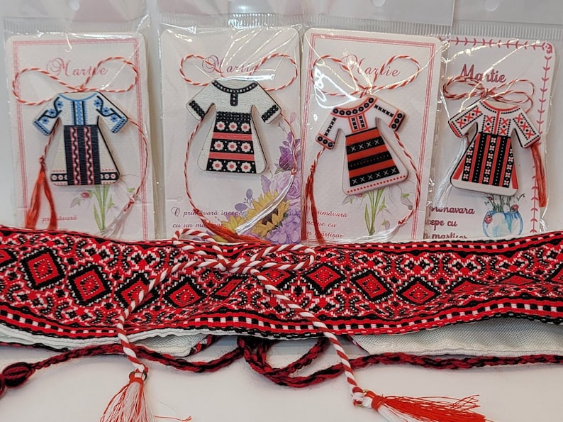 Pode incluir: Quatro ornamentos de madeira feitos &agrave; m&atilde;o em forma de vestidos tradicionais romenos, cada um com um padr&atilde;o bordado diferente. Os ornamentos s&atilde;o presos a cordas vermelhas e brancas com borlas. O texto "Martie" est&aacute; impresso em cada cart&atilde;o.