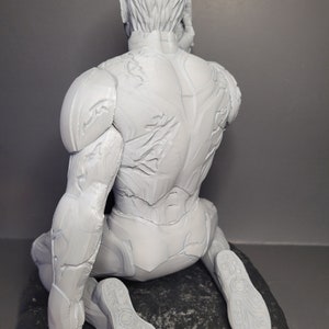 May include: A white 3D printed figurine of a person in a seated pose, wearing a detailed, textured suit. The figurine is sitting on a textured, gray base.