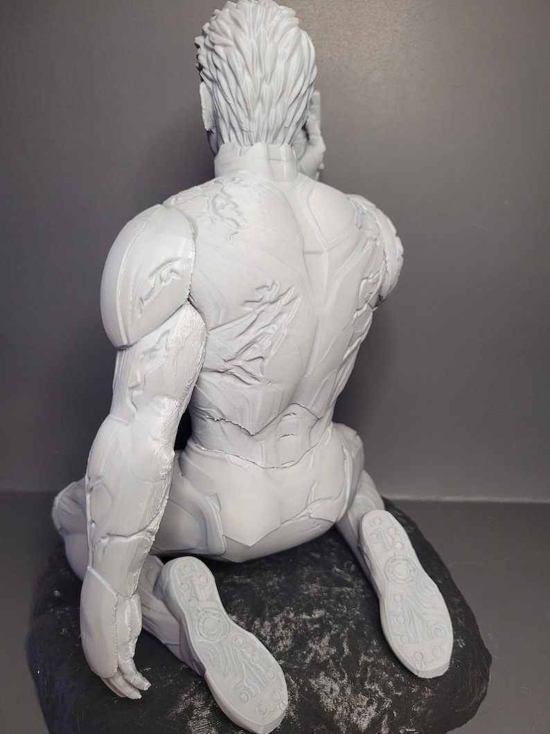 May include: A white 3D printed figurine of a person in a seated pose, wearing a detailed, textured suit. The figurine is sitting on a textured, gray base.