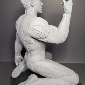 May include: A white 3D printed figurine of a superhero in a kneeling pose. The figurine has a detailed, textured surface and is posed with one arm raised.