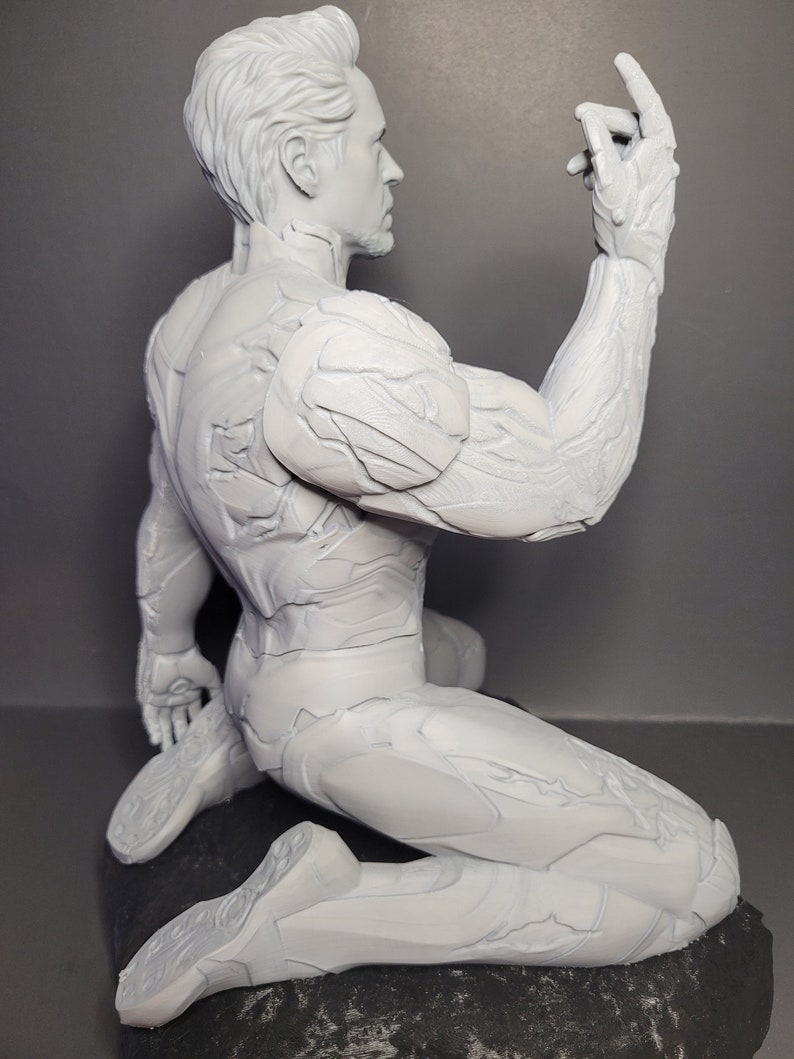 May include: A white 3D printed figurine of a superhero in a kneeling pose. The figurine has a detailed, textured surface and is posed with one arm raised.
