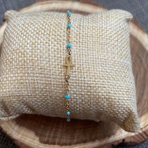 May include: A gold chain bracelet with a turquoise blue bead accent and an ankh charm.