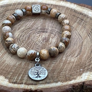 May include: A brown and white stone bracelet with a silver Om charm and a silver tree of life pendant.