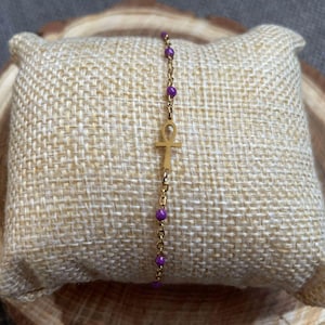 May include: A gold chain bracelet with purple beads and an ankh charm.