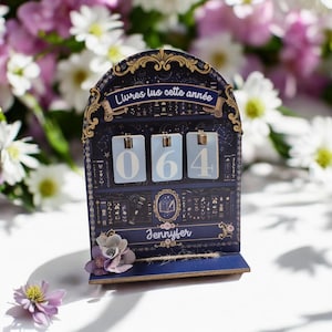 Peut inclure: Un présentoir en bois bleu foncé en forme d'arche portant l'inscription "Livres lus cette année" et "Jennyfer". Il comporte trois plaquettes rectangulaires bleu clair affichant les chiffres 0, 6 et 4, ornées de motifs célestes dorés.