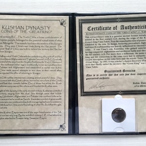 May include: A close-up of a certificate of authenticity for a Kushan Dynasty coin. The certificate is printed on a cream-colored paper with a brown border. The text on the certificate reads "Kushan Dynasty Coins of the "Great King" C. 85 A.D.". The certificate is signed by Robin Danziger, ANA #R164636. The coin is displayed in a clear plastic case.