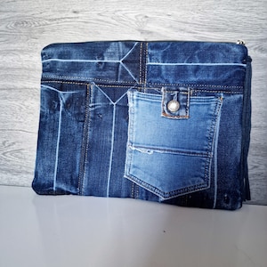 Könnte beinhalten: Eine rechteckige Jeans-Clutch mit Reißverschluss. Die Clutch besteht aus recyceltem Denim und verfügt über eine Tasche und Nähte von Jeans. Die Farbe ist ein mittleres bis dunkles Blau.
