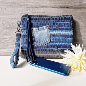 May include: A blue denim clutch bag with a long strap and a fringe detail. The bag has a patch pocket on the front and is made from recycled denim.