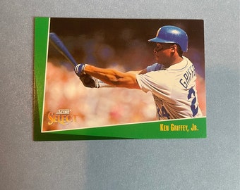 May include: A green, white, and gold baseball card featuring a baseball player in a blue and white uniform swinging a bat. The card has the text "SCORE SELECT" and "Ken Griffey, Jr." printed on it.