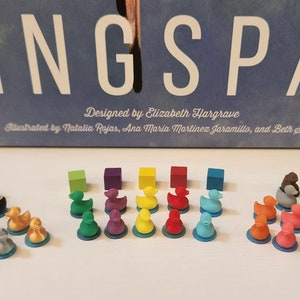 May include: A set of colorful bird meeples for the board game Wingspan. The meeples are made of plastic and come in a variety of colors, including green, purple, yellow, red, blue, orange, brown, black, and white. The meeples are arranged in rows on a white surface.