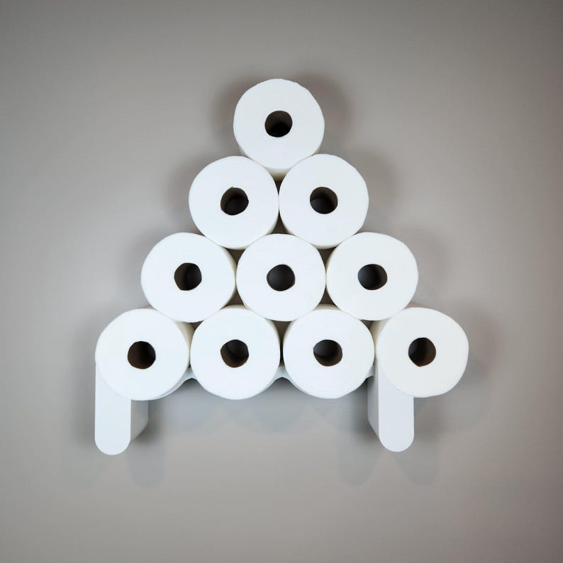 May include: A white, wall-mounted toilet paper holder with a geometric design. The holder is designed to hold nine rolls of white toilet paper, arranged in a pyramid shape. The holder has a minimalist, modern aesthetic.
