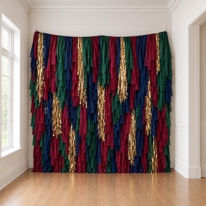 May include: A decorative wall backdrop featuring vertical strips of fabric in deep shades of navy blue, forest green, and burgundy, interspersed with shimmering gold metallic fringe strands hanging from a horizontal rod.