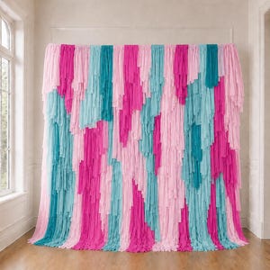 May include: A decorative backdrop featuring vertical strips of fabric in alternating shades of light pink, bright magenta, and turquoise. The fabric strips are layered to create a textured, fringed appearance that hangs from a horizontal rod.