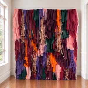 May include: A large decorative backdrop made of layered vertical strips of tissue paper in shades of pink, dark red, purple, orange, and dark green, interspersed with shimmering metallic copper fringe accents hanging from the top edge.