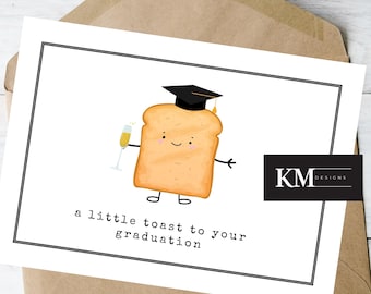 May include: A white card with a black border features a cartoon illustration of a slice of toast wearing a graduation cap and holding a glass of champagne. The text "a little toast to your graduation" is printed below the illustration. The card is signed "KM Designs".