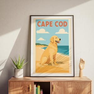 Pode incluir: Um pôster de estilo vintage com o texto "CAPE COD" em letras laranja. O pôster apresenta um cão golden retriever sentado numa praia com água azul e um céu nublado.