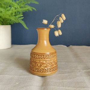 Puede incluir: Un pequeño jarrón de cerámica marrón con un diseño texturizado. El jarrón está lleno de flores secas.