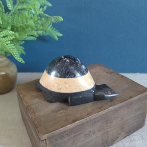 May include: A black and white marble turtle figurine with a brown wooden base. The turtle is carved with intricate details and has a smooth, polished finish.