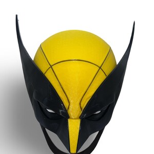 Puede incluir: Una máscara de superhéroe impresa en 3D de color negro y amarillo con una nariz puntiaguda y orejas grandes. La máscara tiene una superficie texturizada y un diseño detallado.
