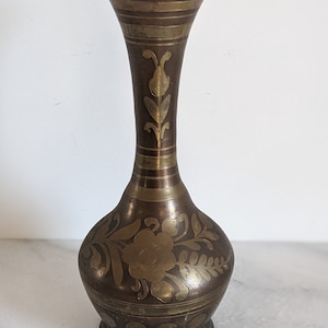 May include: A small, brass vase with an intricate floral design. The vase is a dark brown color with gold accents.