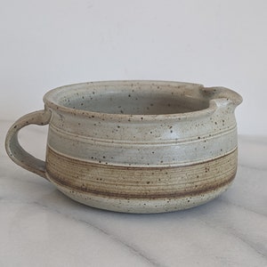 May include: A white ceramic soup bowl with brown stripes and speckles. The bowl has a handle and a spout.